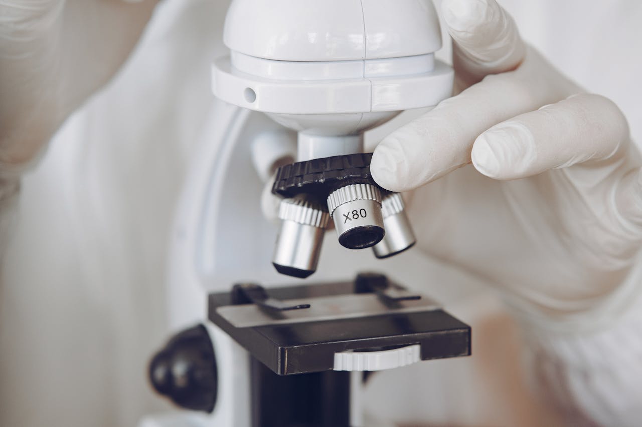 Gloved scientist adjusting a microscope in a laboratory setting, focusing on optics and research.